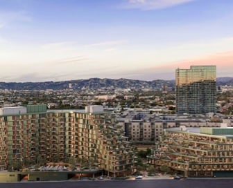 A large, green mixed-use building with angular sides in front of a large mountain range.