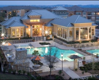 A white, plaster and stone residential clubhouse at dusk with a blue pool in front of it.