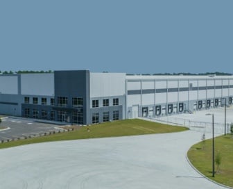 A large blue and white industrial building with an empty parking lot and truck bays in front of it.